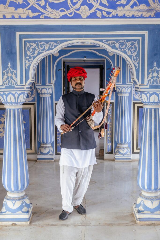 A musician in a red turban outside a blue-painted building in Jaipur