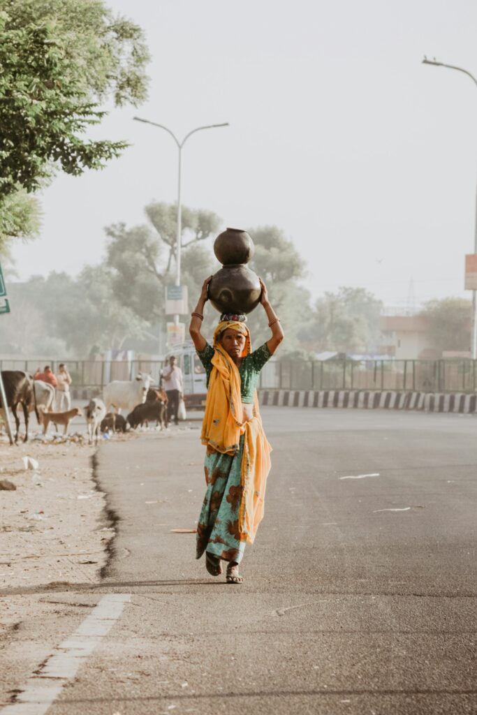 A woman carrying two water pots on her head along a Rajasthan road at dawn